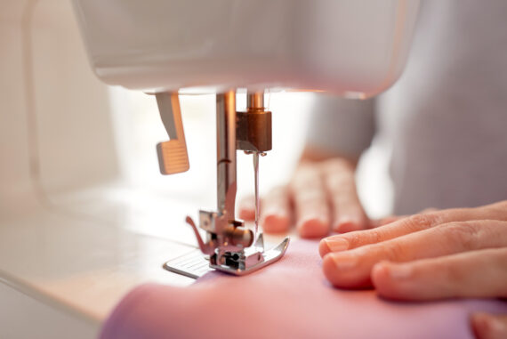 needlework and tailoring concept - sewing machine presser foot stitching fabric